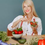 Blonde woman enjoying a fresh salad surrounded by vegetables, promoting healthy eating.